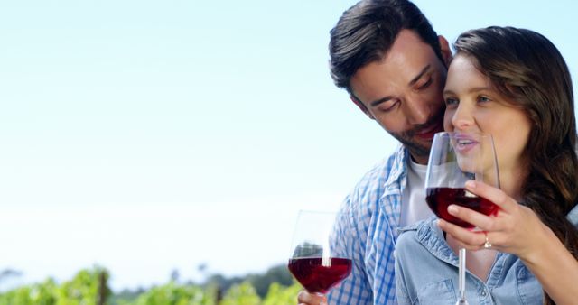 A young Caucasian couple enjoys a glass of wine together in a vineyard, with copy space. Their intimate moment reflects a romantic setting, often associated with leisure and wine tasting experiences.