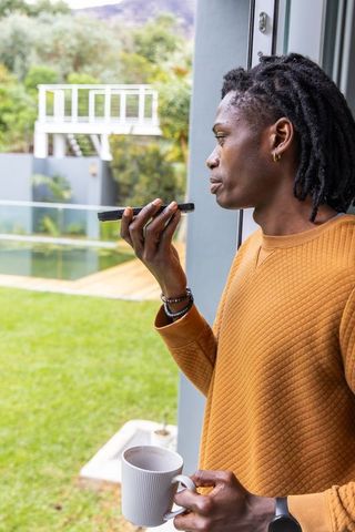 Man speaking into smartphone while holding coffee, overlooking backyard pool and deck