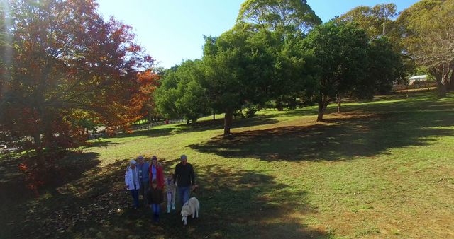 Caucasian grandparents, parents, son and daughter walking with dog in sunny park, copy space. Free time, family, three generation family, togetherness, pets, nature and healthy lifestyle, unaltered.