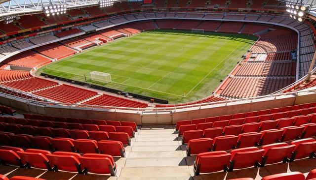 Panoramic empty football stadium with striped green pitch and red seating from main stand