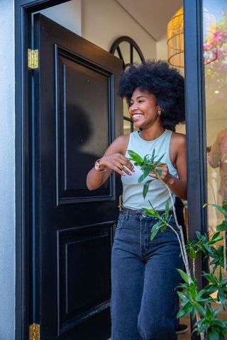 Smiling Woman Standing in Doorway with Potted Plants in Stylish Home