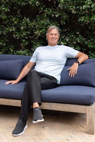 Relaxed senior man lounging on navy outdoor sofa in leafy courtyard