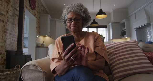 Senior african american woman using smartphone while drinking coffee while sitting on the couch at home. staying at home in self isolation in quarantine lockdown