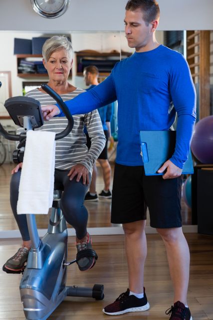 Senior woman receiving guidance from physiotherapist while using exercise bike in clinic. Great for illustrating physical therapy, senior fitness, rehabilitation programs, healthcare routines, and physical training in a clinical setting.