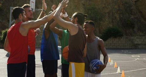 Outdoor basketball team high-fiving at sunset on urban court, diverse players celebrating