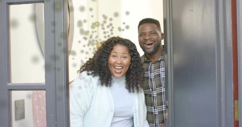 Smiling couple welcoming at open front door with sidelight, warm home entryway