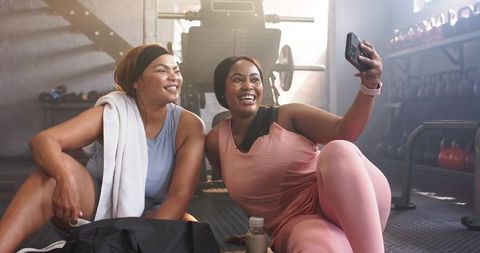 Smiling diverse women taking gym selfie while resting after workout in pastel activewear