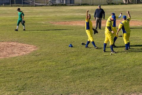 Yellow and blue baseball team celebrating scoring play on community diamond