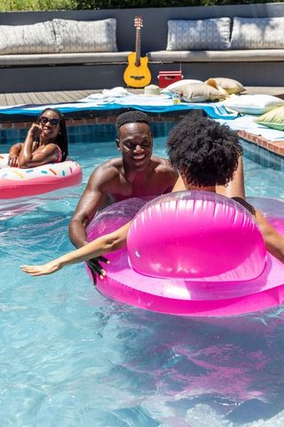 African american friends laughing and holding bright pink inflatable ring in backyard pool