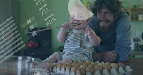 Playful baby mouthing wooden spoon on kitchen counter while smiling father watches carton of eggs
