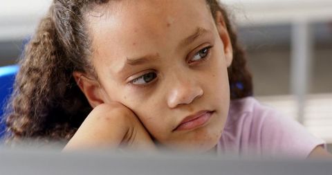 Pensive african american teenage girl resting chin on hand and gazing away in classroom