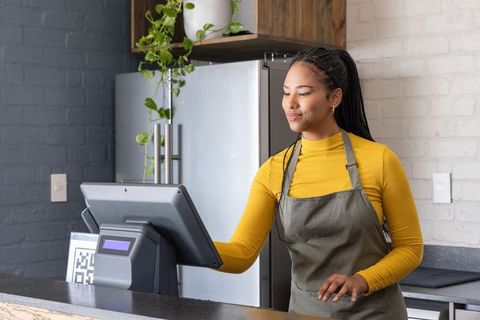 African american barista using touchscreen pos at modern cafe counter with qr code