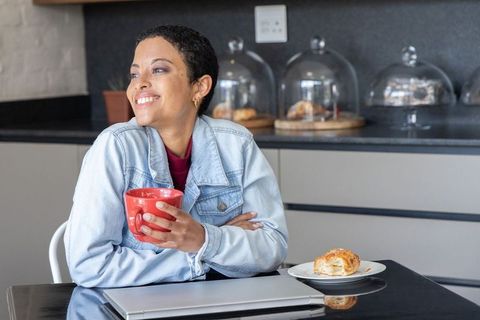 African american woman sipping coffee and smiling near laptop in cozy modern cafe