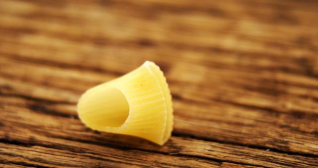 Single dry pasta shell on textured wooden surface, great for illustrating recipes, food blogs, or culinary magazines. Can be used to represent Italian cuisine, cooking ingredients, and kitchen-related content.