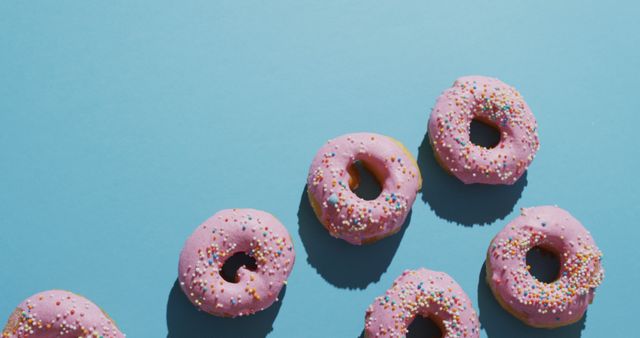 This image shows a vibrant assortment of iced donuts against a striking blue background, making it ideal for use in marketing materials, advertisements, or social media posts related to bakery, dessert shops, or junk food promotions. The combination of bright colors and playful arrangement appeals to both younger demographics and anyone with a sweet tooth, adding a visually appealing and joyful element to any content.