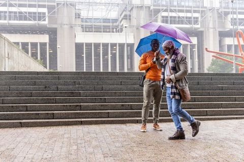 African american men walking down wet urban steps holding blue and purple umbrellas in rain