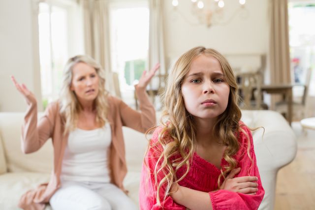 Mother and daughter having a heated argument in a bright living room. The daughter looks upset with arms crossed, while the mother appears frustrated in the background. Useful for illustrating family conflicts, parenting challenges, emotional stress, and communication issues within families.