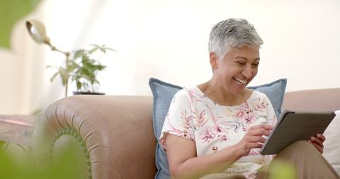 Happy Senior Woman Relaxing on Couch Using Tablet