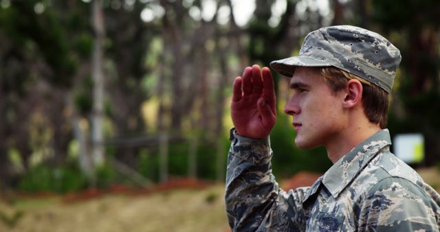 Young male soldier wearing camouflage uniform saluting outdoors. This image is ideal for themes related to military service, honor, dedication, national security, and patriotism. It can be used for articles, websites, or promotional materials emphasizing commitment and discipline in the armed forces.