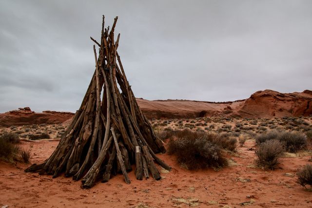 Wooden teepee in a remote desert landscape under a cloudy sky, showcasing the rustic beauty of natural materials and arid environments. Ideal for content related to survival, adventure, indigenous culture, and outdoor activities.