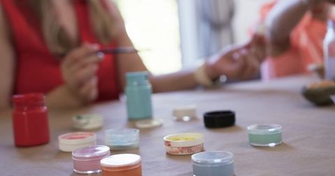 Manicure brush reaching toward hand with pastel nail pigment jars on worktable