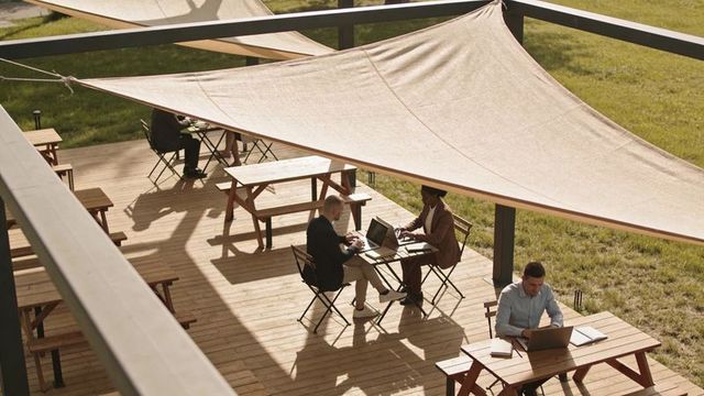 Outdoor coworking professionals working under shade sails on wooden deck patio