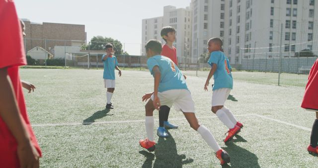 Boys playing an engaging game of soccer on an urban field surrounded by city buildings during the day. An ideal visual representation for topics like youth sports, teamwork, physical fitness, and outdoor activities. Useful for promotional materials for sports programs, physical education content, and urban recreational projects.