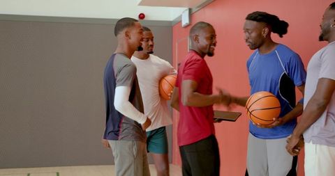 Smiling diverse male basketball teammates greeting and shaking hands with basketballs