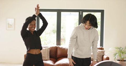 Black woman and asian man stretching in modern living room in casual activewear