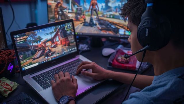 Teenage gamer immersed in video game on laptop with dual screens