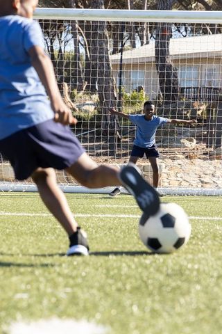 African american boys taking penalty kick with goalkeeper defending goal on sunny turf