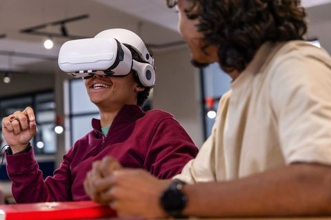 Multicultural students testing VR headset while collaborating in modern tech workspace