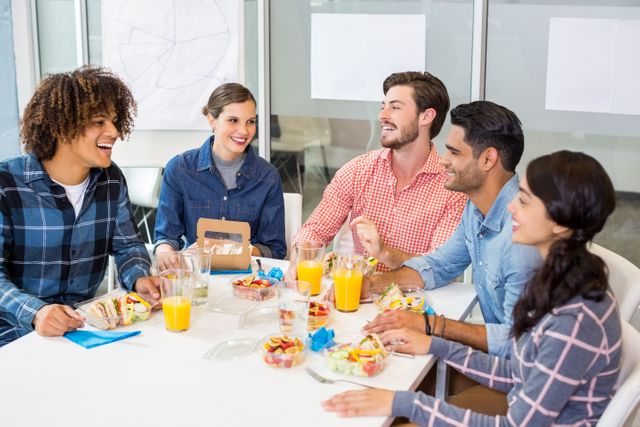 Group of diverse colleagues enjoying breakfast together in a modern office setting. They are smiling, interacting, and sharing food and drinks, creating a friendly and collaborative atmosphere. Ideal for use in business, teamwork, and workplace culture themes, as well as promoting a positive work environment.