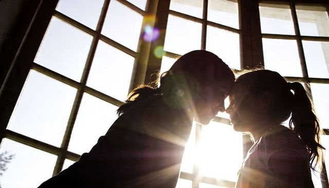 Parent and child sharing tender forehead touch with dramatic backlight and sunburst