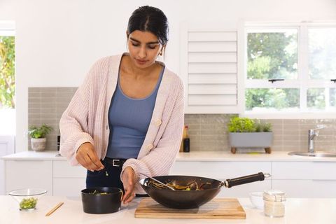 Asian Woman Seasoning Vegetables in Modern Kitchen Interior