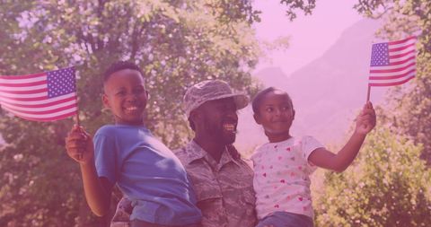 a military father wearing a soldier uniform joyfully enjoys time with his brother and sister outdoors. both children hold american flags, showcasing a sense of patriotism and national pride. this scene reflects themes of family unity, support, and love, perfect for use in family-oriented, patriotic, or military-themed publications highlighting togetherness and support of military families.