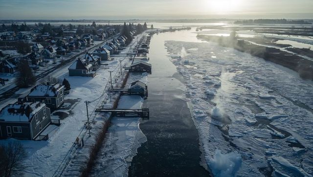 Flowing winter canal with ice floes and snow-covered houses at golden hour