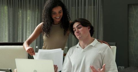 Happy Couple Consulting Documents with Laptop in Living Room