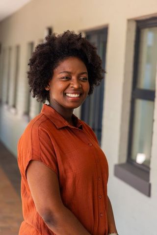 Smiling african american woman standing in corridor wearing rust shirt, confident portrait