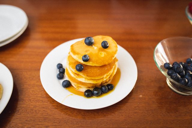 Close-up of stacked pancakes with syrup and blueberries served in plate on table. unaltered, breakfast, sweet food, berry fruit and organic.