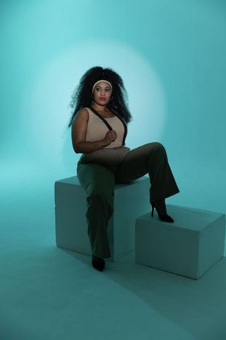 Confident african american woman sitting on blocks in turquoise studio lighting