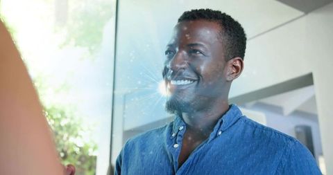 Smiling black man in blue shirt by glass door with sun flare and natural light