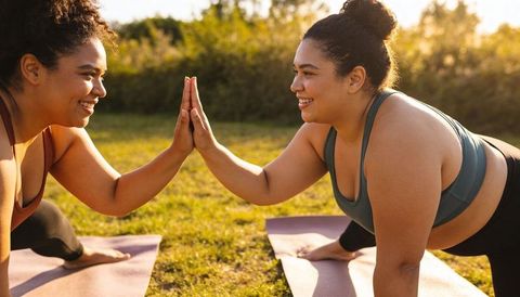 Two women high-fiving during outdoor yoga low-plank lunges at golden hour park