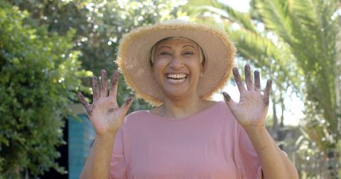 Senior woman in garden joyfully displaying muddy hands on a sunny day