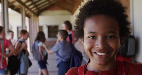 Smiling schoolboy wearing backpack straps standing in sunlit corridor with arched wooden ceiling