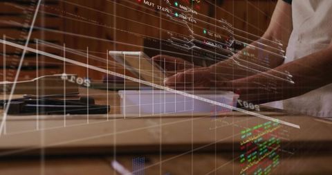 Male tapping tablet on wooden workbench with fintech data overlay and touchscreen interface