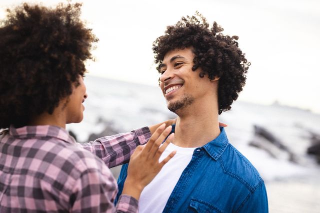 Happy african american afro young couple looking each other face to face while talking at beach. unaltered, lifestyle, love and togetherness concept.