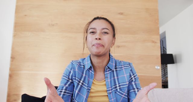 Smiling woman in plaid shirt making hand gestures while sitting on a couch in a cozy indoor setting. Ideal for use in articles or blogs about communication, confidence, home lifestyle, or casual fashion.