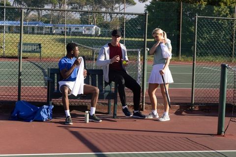 Diverse tennis teammates taking break on court bench between practice sessions