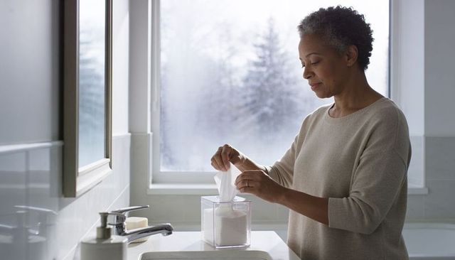 Senior woman taking tissue at bathroom vanity in soft morning light calm self care moment